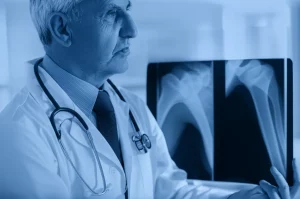 Un medico specialista in reumatologia che illustra a un paziente anziano i benefici del denosumab, mostrando una comparazione tra una radiografia di un'articolazione danneggiata e una più sana. Stile ritratto, obiettivo prime 35mm, duotone blu e grigio per un'atmosfera professionale e rassicurante, profondità di campo.