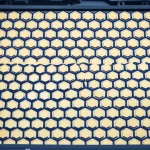 Photorealistic close-up macro shot of a fabricated metasurface array with hexagonal refractive lenses, showing intricate detail of the meta-atoms. Object photography, macro lens, 105mm, high detail, precise focusing, controlled lighting.