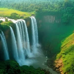 Ampia veduta aerea del paesaggio lussureggiante che circonda le cascate Olumirin (Erin Ijesa) in Nigeria, catturata con un obiettivo grandangolare da 18mm. La luce del mattino illumina la foschia creata dall'acqua, mettendo in risalto la vegetazione vibrante. Fotografia paesaggistica, focus nitido.