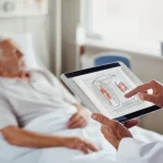 Un medico che consulta un grafico predittivo, simile a un nomogramma, su un tablet, con un paziente anziano visibile ma leggermente sfocato sullo sfondo in un letto di un reparto ospedaliero generale, non di terapia intensiva. Illuminazione naturale da una finestra. Obiettivo da 35mm, colori caldi, profondità di campo che enfatizza il medico e il tablet. Immagine fotorealistica.