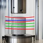 Immagine fotorealistica di un campione cilindrico di arenaria compatta all'interno di una cella triassiale da laboratorio in acciaio lucido. Sovrapposte al campione ci sono linee di forza digitali trasparenti e colorate (rosso, blu, verde) che illustrano diversi percorsi di stress triassiale (compressione isotropa, taglio puro, compressione convenzionale). L'illuminazione è drammatica, focalizzata sul campione, con lo sfondo della macchina di prova leggermente sfocato. Obiettivo prime 35mm, profondità di campo media.