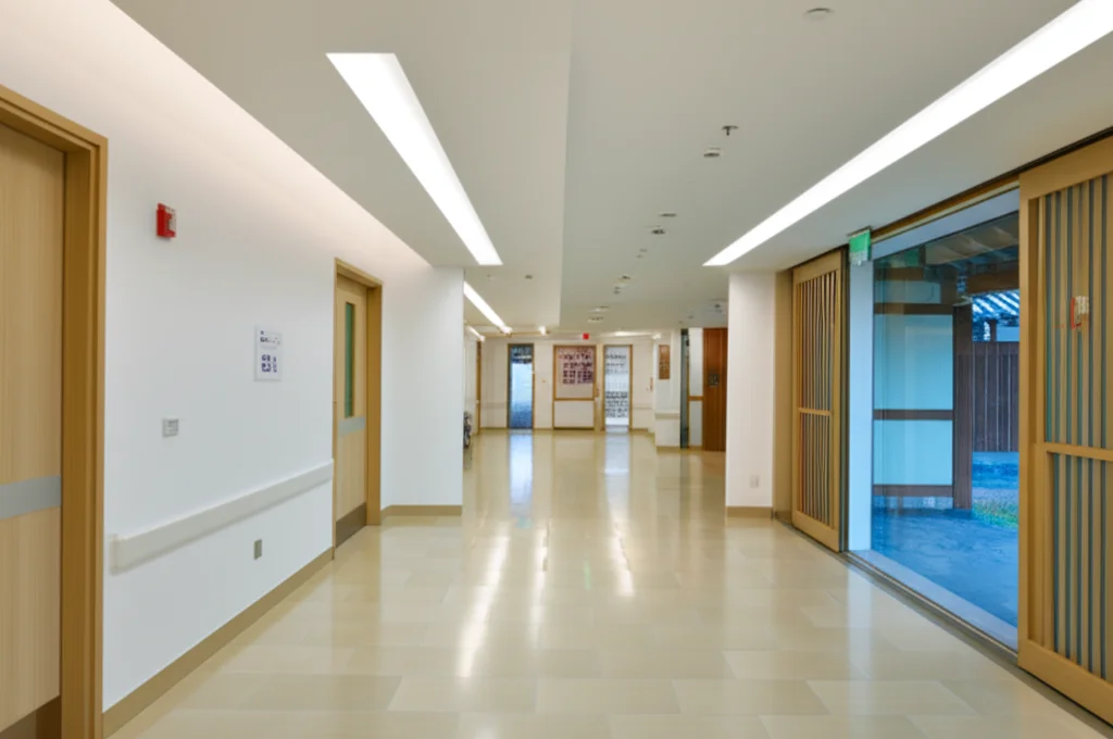 A wide-angle shot inside a modern hospital hallway with subtle traditional Korean architectural elements visible in the background, 24mm lens, natural light filtering through windows.