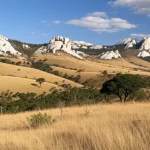 Paesaggio mozzafiato del Massiccio dell'Itremo in Madagascar, con affioramenti rocciosi di quarzite che emergono da praterie ondulate e macchie di foresta di tapia. Obiettivo grandangolare 24mm, luce dorata del tardo pomeriggio, elevata profondità di campo per mostrare la vastità e i dettagli dell'ambiente, cielo con nuvole sparse.
