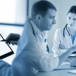 Un'immagine composita che mostra da un lato un paziente che compila un sondaggio online su un tablet e dall'altro un team medico multidisciplinare (reumatologo, infermiere) che discute i risultati di un PREM. L'immagine deve trasmettere collaborazione e centralità del paziente. Prime lens, 35mm, duotone blu e grigio, depth of field.