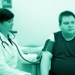 Un medico che utilizza un dispositivo di oscillometria a impulsi (IOS) su un paziente obeso in un ambiente clinico. L'immagine è un ritratto con obiettivo da 35mm, con una profondità di campo che sfoca leggermente lo sfondo, e utilizza una palette di colori duotone verde acqua e grigio per un aspetto professionale e moderno.