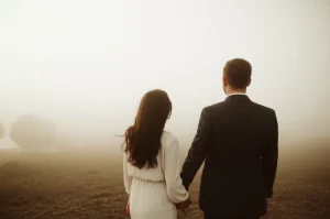 A couple looking towards a hazy horizon, holding hands, symbolizing navigating uncertainty together. 35mm portrait, depth of field, controlled lighting.