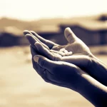 Immagine fotorealistica di forte impatto emotivo: una mano tesa che offre una compressa antiretrovirale a un'altra mano in un contesto rurale dell'Africa subsahariana, simboleggiando la speranza e la sfida dell'accesso alle cure. Obiettivo prime 35mm, luce soffusa e calda, profondità di campo che mette a fuoco le mani e la compressa, con lo sfondo leggermente sfocato che suggerisce un villaggio. Toni seppia e blu duotone per un effetto intenso ma speranzoso.