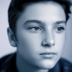 A close-up 35mm portrait of a thoughtful adolescent looking slightly off-camera, depth of field, subtle blue and grey duotones, conveying vulnerability.