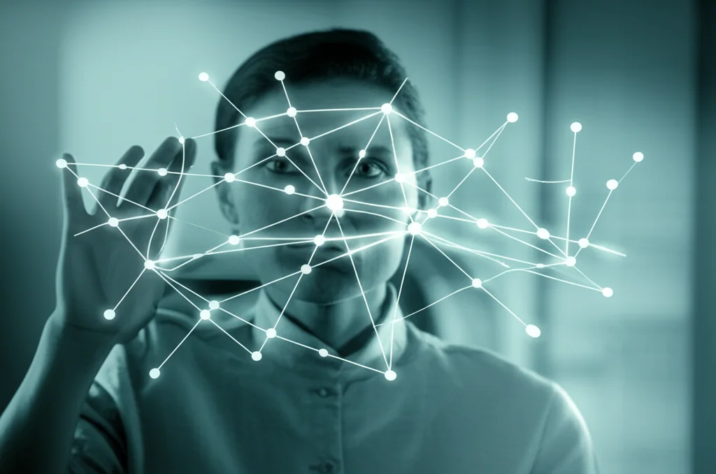 Persona in un ambiente sereno e luminoso, che guarda con espressione concentrata ma calma un diagramma astratto di connessioni neurali proiettato olograficamente davanti a sé. L'immagine simboleggia la comprensione e la gestione attiva dei propri pensieri. Obiettivo prime da 35mm, profondità di campo che sfoca leggermente lo sfondo, duotone sui toni del blu e del verde acqua per un'atmosfera calma e tecnologica.