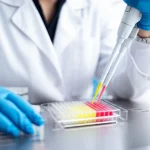 Fotografia realistica di un ricercatore in camice bianco che utilizza una pipetta multicanale per aggiungere un liquido colorato a una piastra TurboCapture a 96 pozzetti in un laboratorio di biologia molecolare luminoso e moderno. Messa a fuoco sulla piastra e sulla punta della pipetta, sfondo leggermente sfocato. Obiettivo prime 35mm, profondità di campo, illuminazione controllata brillante.