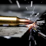 Primo piano di un proiettile ad alta velocità che sta per impattare una spessa lastra di metallo, con scintille e frammenti che iniziano a staccarsi dalla superficie al punto di impatto. Obiettivo teleobiettivo zoom 200mm, alta velocità dell'otturatore per congelare l'azione, tracciamento del movimento, illuminazione drammatica laterale per esaltare texture e deformazione, bianco e nero con un singolo colore d'accento per le scintille.