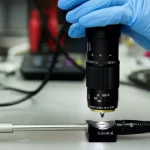 Immagine fotorealistica di un campione di roccia carbonatica bioturbata in laboratorio, con un permeametro portatile che effettua una misurazione spot sulla sua superficie. Macro lens, 60mm, high detail, precise focusing, controlled lighting per evidenziare la texture della roccia e lo strumento.