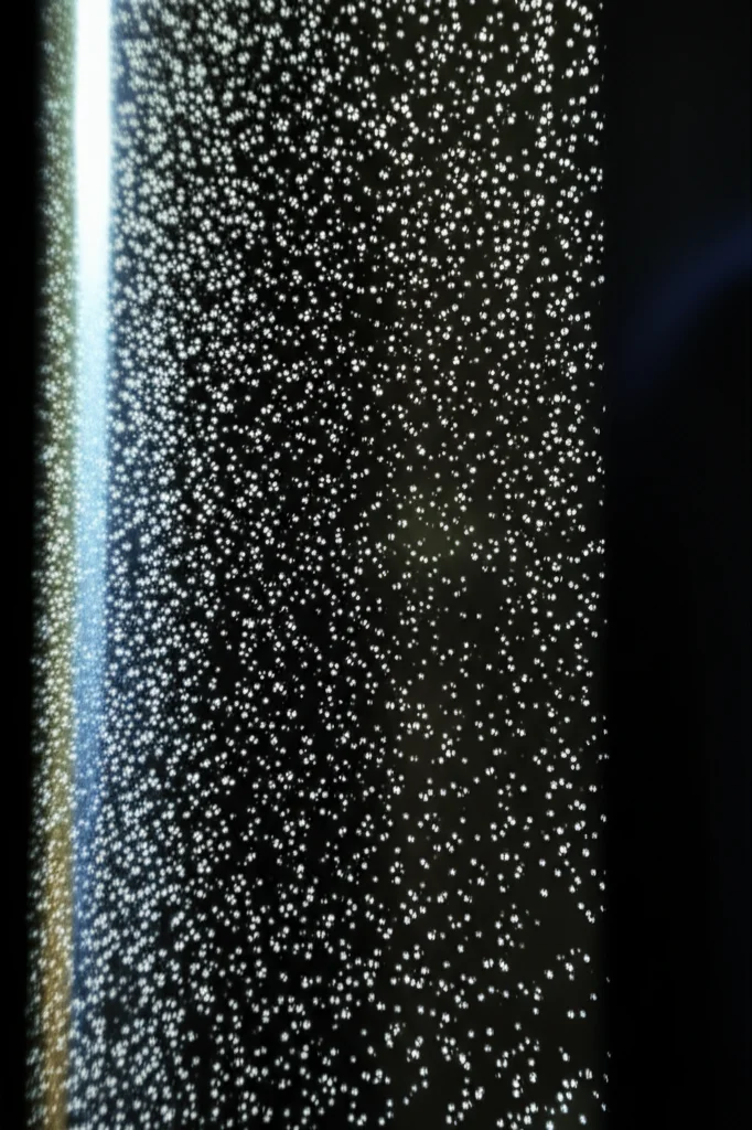 Immagine macro, lente 80mm, che mostra particelle di PM10 sospese nell'aria, illuminate da un raggio di luce solare che filtra attraverso una finestra, con uno sfondo leggermente sfocato di un ambiente domestico per suggerire l'esposizione quotidiana. Alta definizione, illuminazione controllata per evidenziare le particelle.