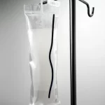 Fotografia macro di un oggetto filamentoso scuro simile a un verme all'interno di una sacca di raccolta urine trasparente appesa a un supporto metallico in ambiente ospedaliero, obiettivo macro 90mm, alta definizione, illuminazione clinica controllata.