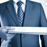 Ritratto fotografico, stile duotone blu e grigio, di una mano che offre un contratto di lavoro a una persona la cui espressione è incerta, simboleggiando il potere di mercato del lavoro e la negoziazione salariale in Spagna. Obiettivo 35mm, profondità di campo. People (portraits), Prime, zoom 24-35mm, duotone (blue and grey), Depth of field.