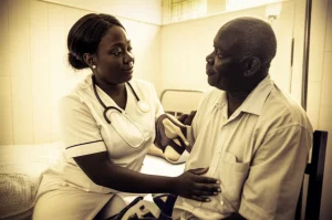 Fotografia ritrattistica di un'infermiera ghanese compassionevole che interagisce con delicatezza con un paziente anziano che ha subito un'amputazione. Obiettivo da 35mm, profondità di campo. La scena è ambientata in una stanza d'ospedale modesta ma pulita in Ghana. Bicromia, magari seppia e crema, per evocare calore ed empatia nonostante la difficile situazione, con focus sull'interazione e le espressioni.