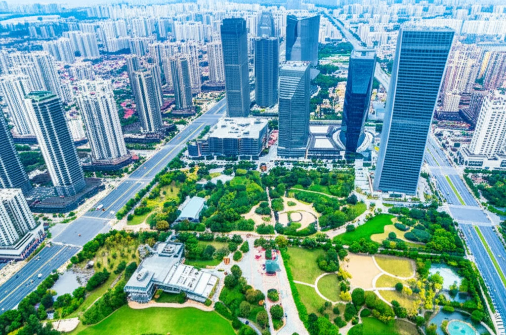 Fotografia aerea, obiettivo zoom 35mm, di una città cinese moderna con grattacieli e infrastrutture turistiche (hotel, attrazioni) integrate armoniosamente con ampi spazi verdi e parchi, a simboleggiare l'influenza positiva dei fattori economici e turistici sul CCD.