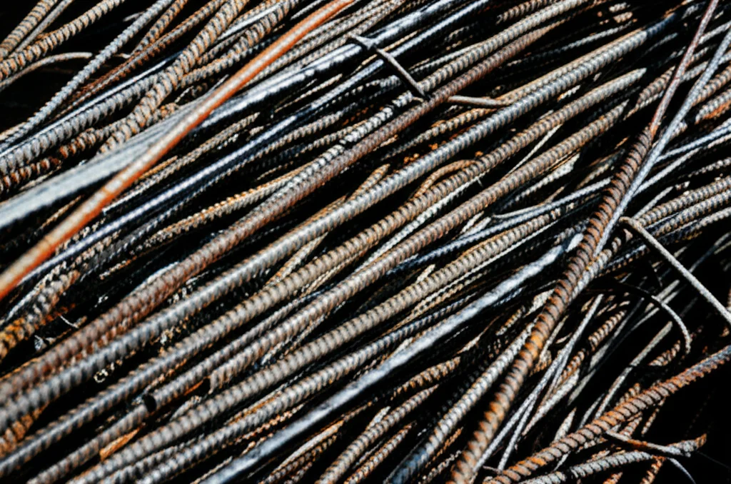 Una montagna di detriti edili, mattoni rotti, cemento sbriciolato e tondini di ferro arrugginiti, accumulati in un cantiere di demolizione a Dhaka. Fotografia di oggetti, obiettivo macro da 90mm, alta definizione, illuminazione controllata per evidenziare la texture e la varietà dei materiali di scarto.