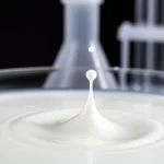 Fotografia macro ad alta definizione di una goccia di latte che cade in un contenitore di vetro da laboratorio, illuminazione controllata, focus preciso sulla texture del latte, con sfondo sfocato di attrezzatura scientifica, obiettivo macro 100mm.