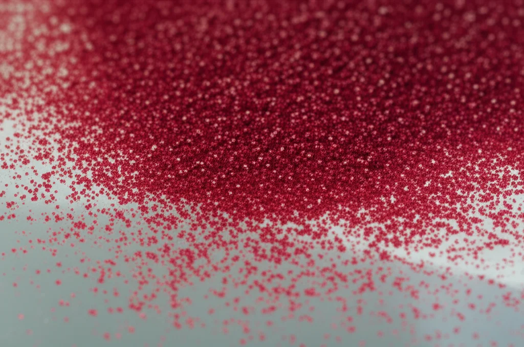 Immagine macro ad alta definizione di polvere di buccia di melograno di colore rosso rubino intenso, con alcune particelle che sembrano brillare leggermente per suggerire la nanodimensione, disposte su una superficie di vetro pulita da laboratorio. Illuminazione controllata e precisa per evidenziare la texture fine della polvere, obiettivo macro 105mm, alta definizione dei dettagli.