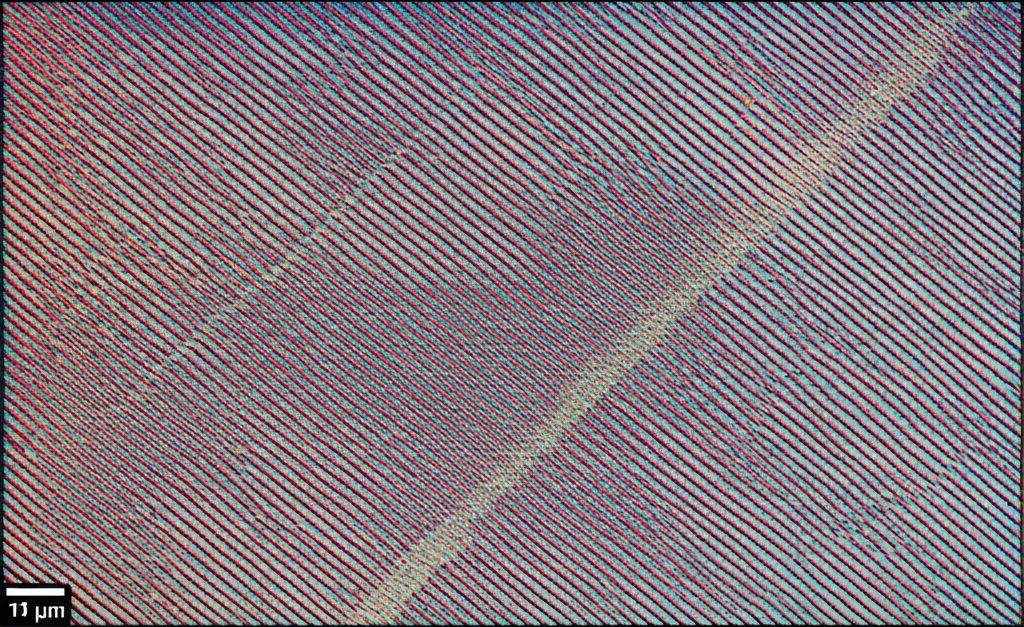Immagine macro di un film sottile di Hf0.5Zr0.5O2 depositato su un substrato di TiN con diverse orientazioni cristalline visibili, obiettivo macro 80mm, alta definizione, messa a fuoco precisa, illuminazione da laboratorio controllata che evidenzia la struttura cristallina e l'interfaccia tra i materiali, con un accenno schematico alle dislocazioni periodiche all'interfaccia.