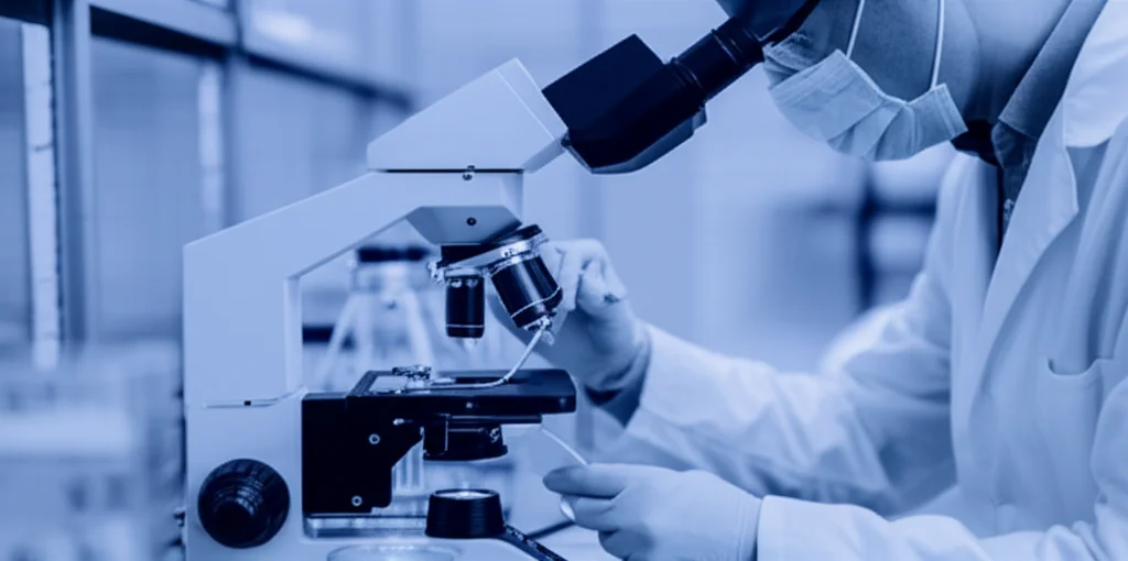 Fotografia di un laboratorio di fecondazione in vitro, lente prime 35mm, con un embriologo che lavora con una pipetta sotto un microscopio, luci soffuse e focus sull'azione precisa, effetto duotone blu e grigio per un'atmosfera scientifica e concentrata.