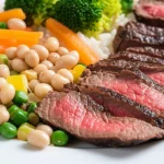 Un'immagine still life con macro lens da 100mm che mostra un piatto bilanciato: una piccola porzione di carne rossa affiancata da una generosa e colorata porzione di verdure fresche, legumi e cereali integrali, con illuminazione controllata e alta definizione dei dettagli, a simboleggiare la sostituzione parziale.