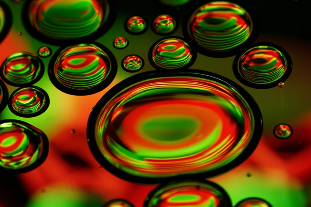 Un primo piano macro di gocce di petrolio greggio su una superficie lucida che riflette grafici azionari digitali di colore verde e rosso. Obiettivo macro da 100mm, illuminazione controllata per evidenziare la texture del petrolio e i riflessi, alta definizione.