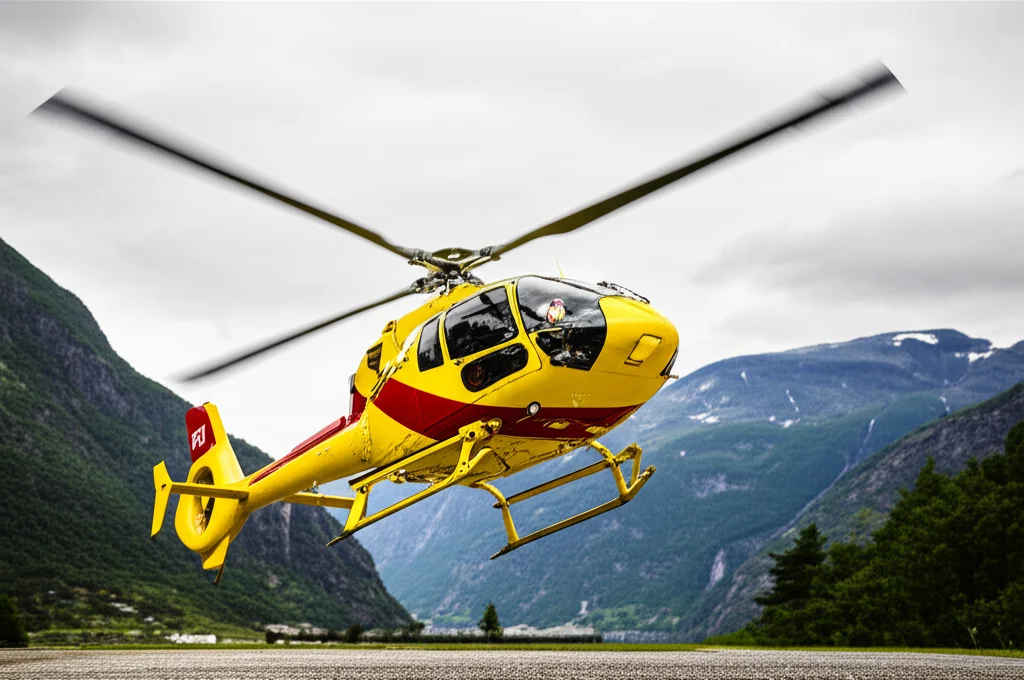 Scatto d'azione di un elicottero HEMS norvegese (modello Airbus H145, di colore giallo e rosso tipico dei servizi di soccorso nordici) in fase di decollo da una base operativa, con un paesaggio di fiordi e montagne norvegesi sullo sfondo in una giornata con cielo parzialmente nuvoloso. Obiettivo telephoto zoom, 200mm, fast shutter speed per congelare il movimento delle pale dell'elicottero, luce naturale diffusa.