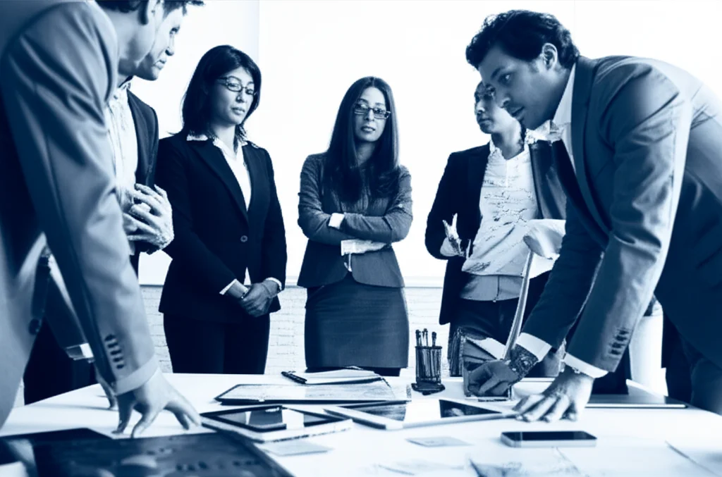 Un gruppo eterogeneo di persone, alcune in abiti da startup casual e altre in abiti corporate formali, che discutono animatamente attorno a un tavolo con post-it e lavagne digitali, 35mm portrait, duotone blu e grigio, a simboleggiare le sfide umane e organizzative nella collaborazione per la trasformazione digitale.