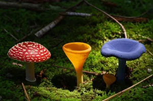 Tre funghi selvatici diversi - uno rosso vivo con macchie bianche (Amanita), uno giallo dorato a forma di trombetta (Cantharellus), uno blu indaco intenso (Lactarius indigo) - che crescono vicini nel muschio verde brillante della foresta pluviale di Oaxaca, illuminati da un suggestivo raggio di sole che filtra tra le foglie. Macro lens, 90mm, high detail, precise focusing, luce naturale drammatica e contrastata.