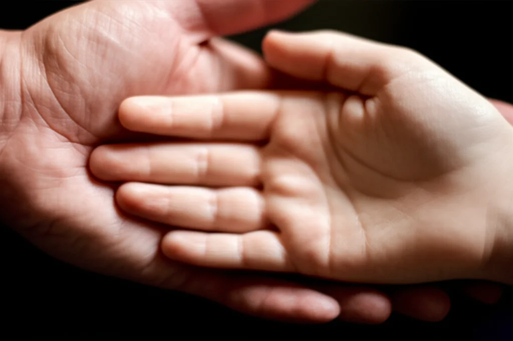 Fotografia macro di due mani, una adulta e una di bambino, quasi che si toccano ma non del tutto, simboleggiando la discrepanza percettiva tra genitori e figli. Obiettivo macro 90mm, illuminazione controllata, alta definizione, focus preciso sulla distanza tra le mani.