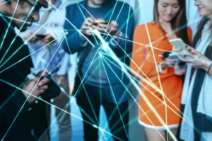 Rappresentazione fotorealistica di una complessa rete luminosa che simboleggia le opinioni sociali, sovrapposta a un gruppo diversificato di persone che guardano i loro smartphone. Obiettivo prime 24mm, profondità di campo, tonalità duotone blu e arancione, a simboleggiare la fusione tra tecnologia e interazione umana.