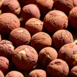Fotografia still life con obiettivo macro 90mm, che mostra in primo piano le palline di argilla espansa leggera (LECA) prodotte con residui di foglie di cajeput, evidenziando la loro texture porosa rosso-mattone e la leggerezza, con illuminazione controllata per massimizzare i dettagli.