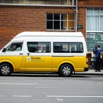 A minibus taxi parked at a busy rank in Durban on a hot day, showing passengers waiting, wide-angle 24mm, depth of field.