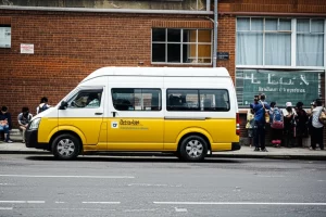 A minibus taxi parked at a busy rank in Durban on a hot day, showing passengers waiting, wide-angle 24mm, depth of field.