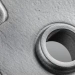 Primo piano fotorealistico di un componente complesso in lega di titanio Ti6Al4V stampato in 3D, con una texture superficiale leggermente ruvida tipica della PBF-LB/M, illuminazione da studio controllata, obiettivo macro 90mm, alta definizione.