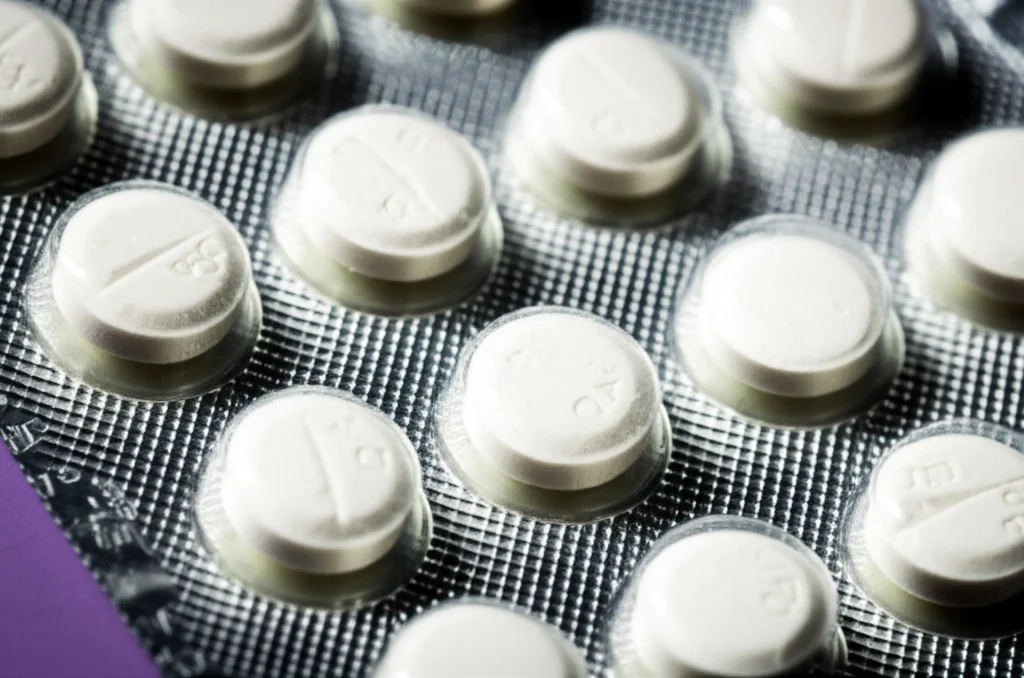 Primo piano di compresse di aspirina a basso dosaggio (75mg) su un blister farmaceutico, illuminazione da studio controllata, obiettivo macro 90mm, alta definizione dei dettagli sulla superficie della compressa e del blister.