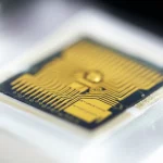 A macro lens shot at 80mm showing a detailed view of a small, intricate biosensor chip with gold plating, positioned on a sterile white surface under controlled lighting, emphasizing the precise engineering.