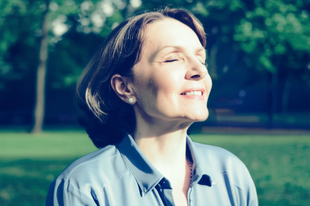 Ritratto fotografico di una persona di mezza età che respira profondamente all'aperto in un parco, simboleggiando la salute polmonare e mentale. Obiettivo 35mm, stile film noir con duotono blu e grigio, profondità di campo.