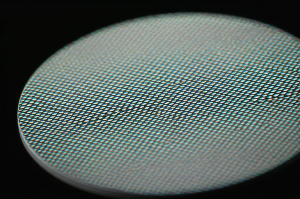 Immagine macro fotorealistica di un wafer di semiconduttore ScAlN su un supporto da laboratorio, illuminazione controllata che evidenzia la texture superficiale e i dettagli cristallini. Macro lens, 80mm, high detail, precise focusing, controlled lighting.