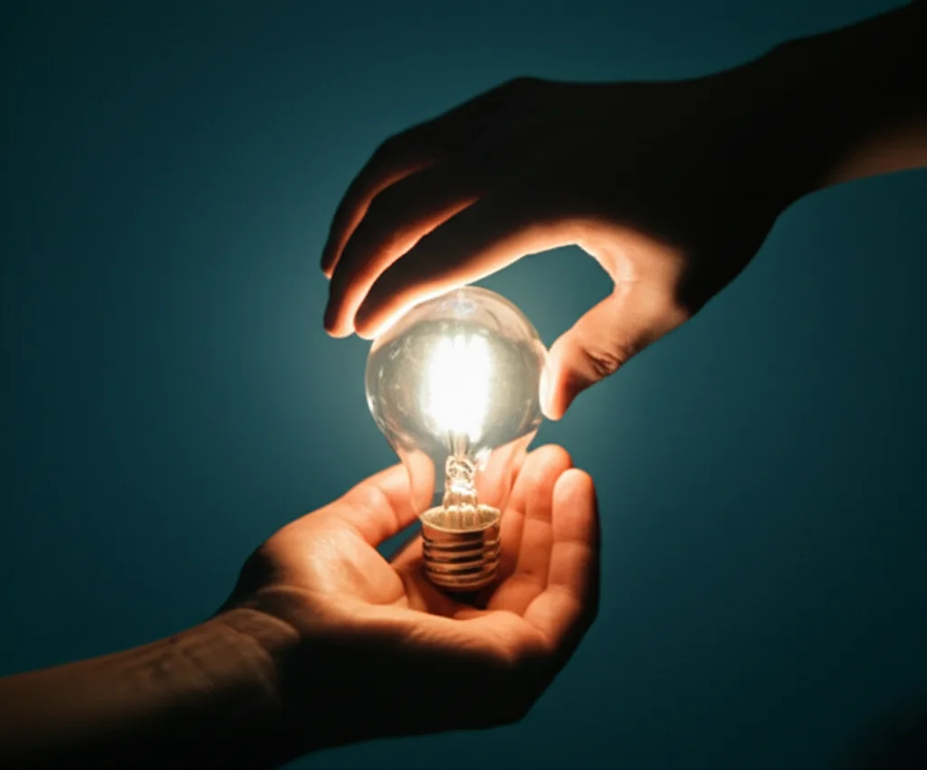 Fotografia macro con obiettivo da 100mm, alta definizione e illuminazione controllata, che mostra due mani che si scambiano una lampadina luminosa, simbolo di un'idea e della collaborazione in ReS tra PMI.