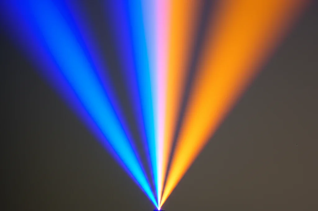 Immagine fotorealistica, obiettivo primario 35mm, profondità di campo, che mostra due distinti flussi di luce, uno blu, uno arancione (bicromia), che si fondono sinergicamente in un fascio combinato più luminoso su uno sfondo neutro.