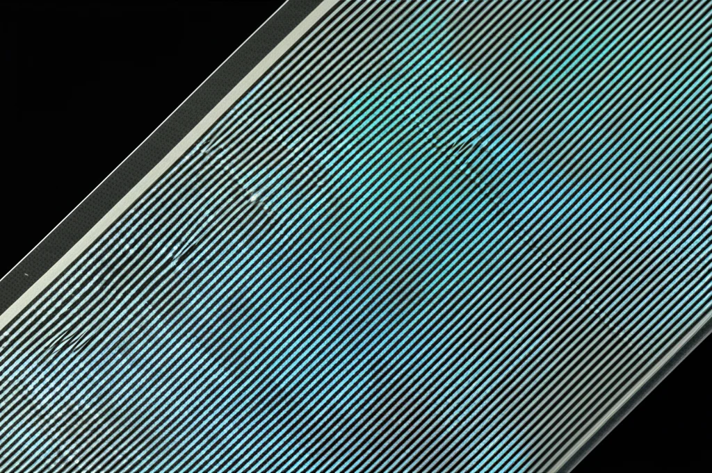 Macro fotografia, obiettivo 80mm, di un foglio flessibile e trasparente con pattern di strutture metalliche microscopiche (simili all'ITO), leggermente piegato. Illuminazione controllata che evidenzia la trasparenza e il pattern intricato. Alto dettaglio, messa a fuoco precisa.