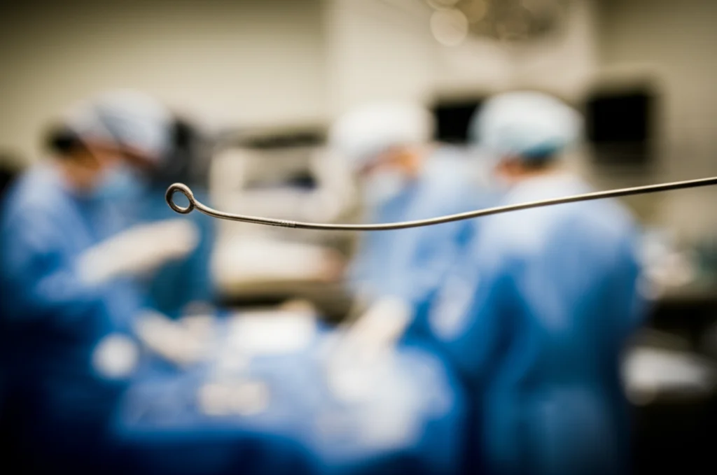 Fotografia medica che mostra, in primo piano, la punta di un filo guida medico flessibile (tipo BMW) leggermente attorcigliato, con profondità di campo ridotta per sfocare lo sfondo di una sala operatoria, stile documentaristico.