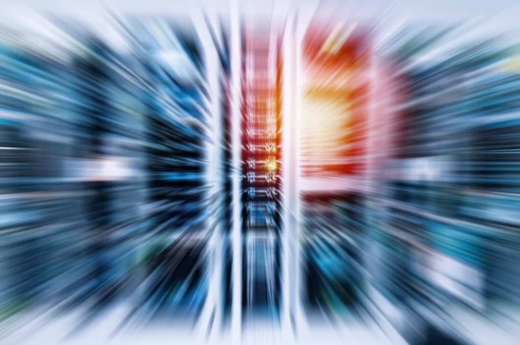 A telephoto zoom shot, 100mm, showing a blur of activity in a hospital IT department with servers and monitors, suggesting complex system management, fast shutter speed, high detail.