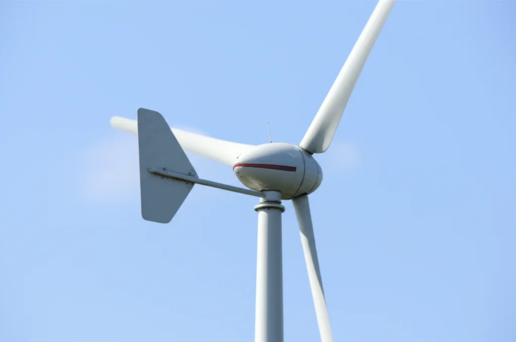 A photorealistic image of a micro wind turbine, focusing on the rotor and tower base. Use a wide-angle lens at 24mm to capture both the turbine and a hint of its surroundings, emphasizing the scale. Include details like sharp focus on the turbine structure and controlled lighting to highlight its mechanical details.