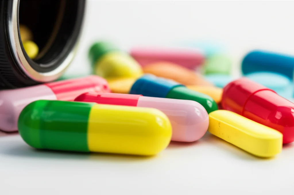 Macro lens, 100mm, high detail, precise focusing on a collection of colorful antibiotic pills and capsules spilled on a sterile white surface.