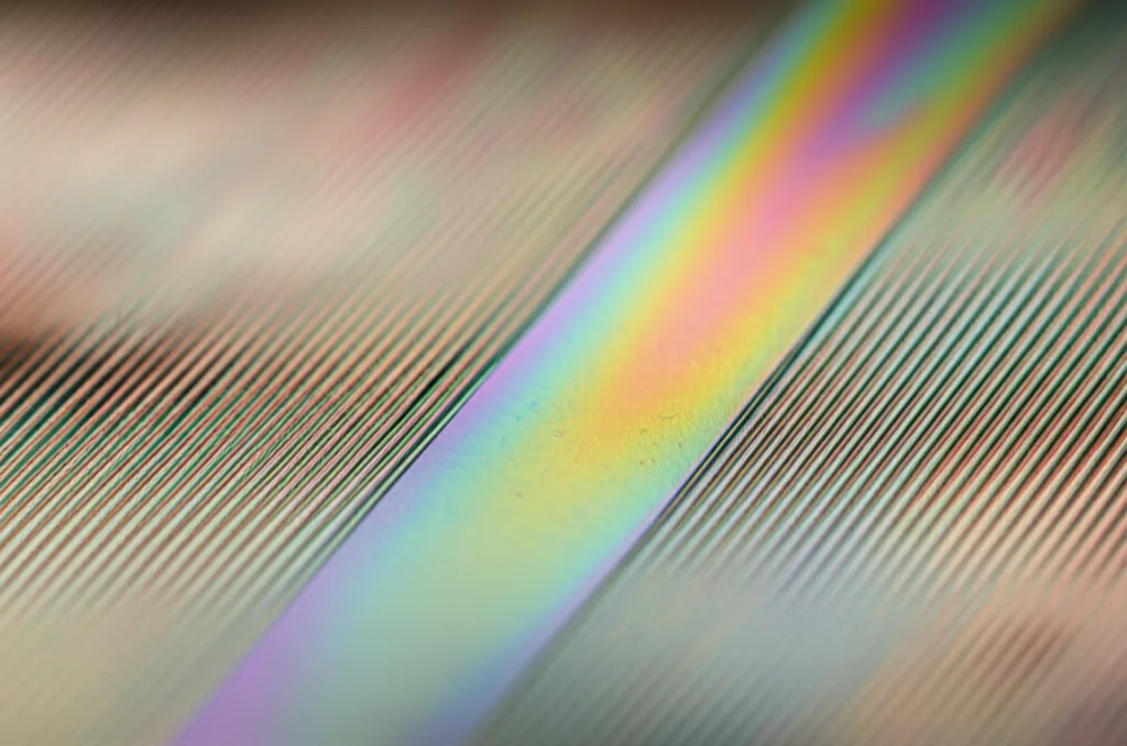 Macro photograph, 80mm lens, of a gleaming metallic thin film being gently bent. The image should show subtle stress lines and rainbow-like interference patterns on its surface due to the strain. Controlled studio lighting with high detail and precise focusing, highlighting the texture of the metal.