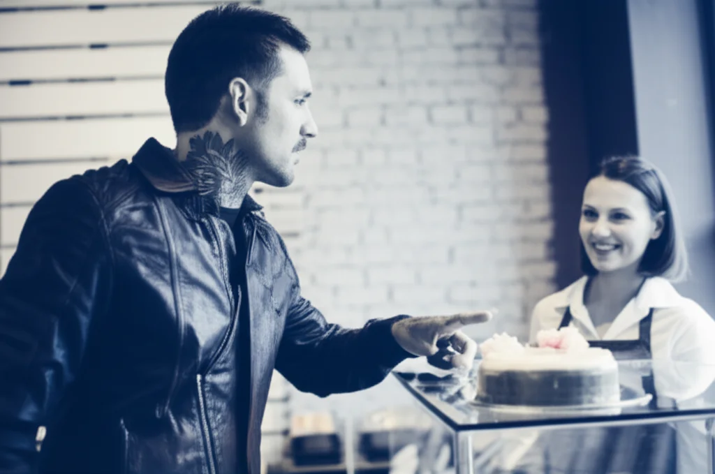 Photorealistic image of a seemingly tough person ordering a delicate pastry in a public setting, 35mm portrait lens, depth of field, blue and grey duotones, capturing the unexpected nature of the action.